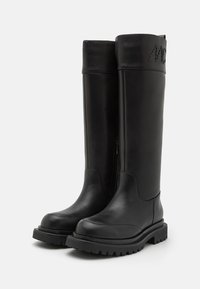 Botas negras hasta la rodilla de cuero suave, con cremallera lateral, suela gruesa con buen agarre y puntera redondeada. Presenta detalles texturizados en la parte superior.