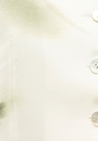 Hemd mit Knopfleiste aus leichtem cremefarbenem Stoff mit subtilen grünen Aquarellmustern. Verfügt über perlmuttfarbene Knöpfe und eine glatte Textur.