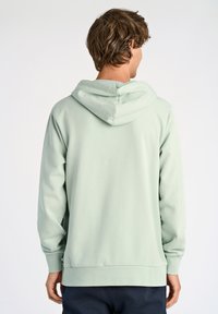 Sudadera verde claro con capucha ajustable, puños acanalados y dobladillo. Tela suave y texturizada con un diseño minimalista, vista desde la parte de atrás.