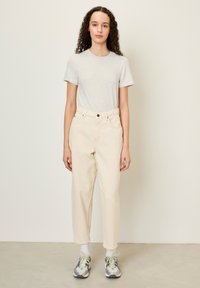 T-shirt gris clair associé à un jean droit taille haute de couleur crème. Le modèle porte des baskets grises avec des accents verts et des chaussettes blanches.