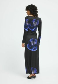 Langes schwarzes Kleid mit blauer Blumenmuster, mit langen Ärmeln und taillierter Silhouette. Glatte Textur, getragen mit schwarzen High Heels.
