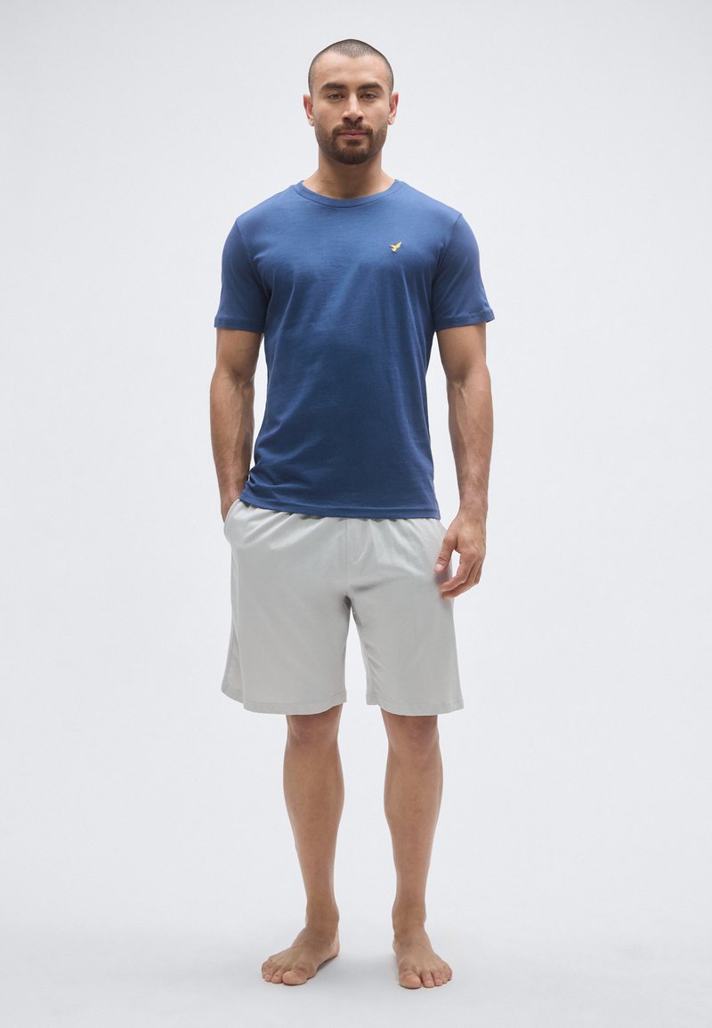 T-shirt en coton bleu à manches courtes et col rond, associé à un short gris clair arrivant au genou ; les deux sont décontractés et confortables.