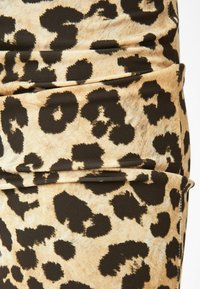 Leopardmönstrad tyg med svarta fläckar på en ljusbrun bakgrund, med en mjuk, elastisk textur och rynkade detaljer.