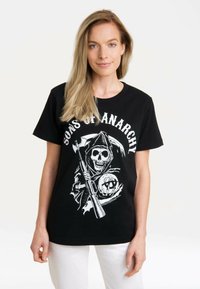 Black cotton t-shirt featuring a graphic of a skull in a hooded cloak, holding a weapon, with the text "Sons of Anarchy" in white above.