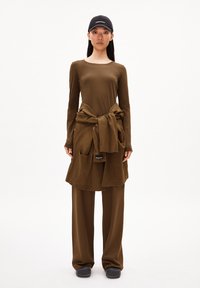 Bruine lange mouwen top gecombineerd met een tuniek met zakken, met een strik in de taille, en bijpassende wijde broek. Zwarte pet met tekstaccenten.