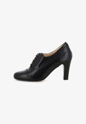 Scarpa nera in pelle con tacco alto, caratterizzata da una punta arrotondata, laccio anteriore e cuciture decorative lungo la parte frontale e i lati.