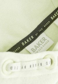 Uzum sati svijetlozelene tkanine s oznakama brenda "Baker by Ted Baker" i odgovarajućim vezicama za cipele provučenim kroz rupice.