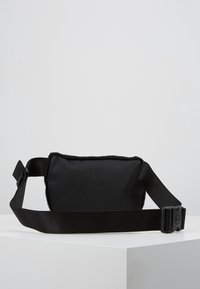 Czarna torba wykonana z miękkiego materiału o gładkiej fakturze. Wyposażona w szeroki, regulowany pasek oraz plastikową klamrę. Kompaktowy, prostokątny kształt.