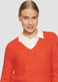V-Ausschnitt, locker sitzender Pullover aus leuchtend orangefarbenem Strickstoff. Über einem weißen Hemd mit Kragen getragen; strukturiert mit einem dezenten Muster.