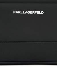 Fekete kiegészítő, amelyen a "KARL LAGERFELD" név fehér szöveggel szerepel. Simává varrt anyag, finom varrásmintával az alszínen.