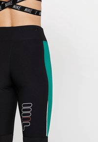 Czarne legginsy z turkusowym bocznym panelem, z nadrukowanym logo w białym i bordowym kolorze. Wykonane z rozciągliwego, teksturowanego materiału.