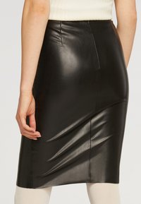 Svart fuskleder pennkjol med en jämn textur, med en mitt bak-seam och subtila veck för en figurnära design.