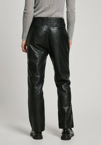 Black leather pants with a sleek design, featuring a high waist, straight leg, and minimalistic back pockets. Smooth texture and shiny finish.