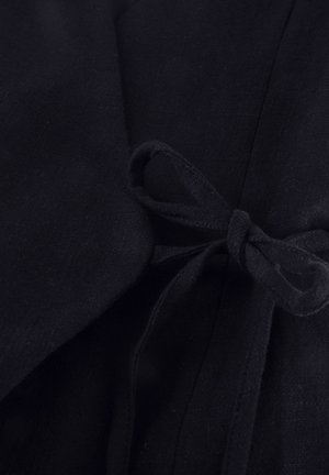 Nahaufnahme eines schwarzen Stoffgürtels, der als Schleife an einem dunklen Kleidungsstück gebunden ist, mit sichtbaren Textur- und Nahtdetails.