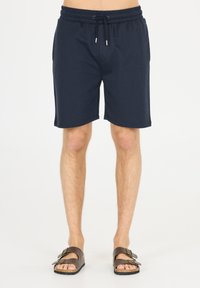 Mörkblå shorts med elastisk midja och snörning, tillverkade av mjukt tyg och med sidfickor, tillsammans med bruna sandaler.