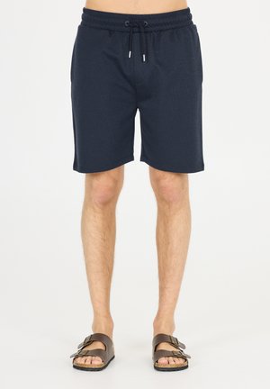 Mørkeblå shorts med elastisk talje og snøre, der har glat stof og sidelommer, parret med brune sandaler.