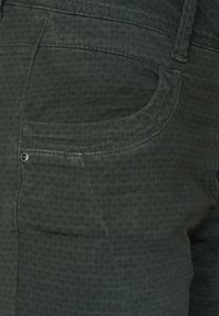 Tmavě zelená látka s vzorem a texturovaným povrchem. Obsahuje boční kapsu s malým kovovým akcentem blízko švu.