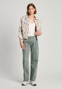 Blomsterprydd denimjakke i lys beige over en hvit v-hals skjorte. Olivengrønne cargo-bukser med sidelommer og hvite sneakers.