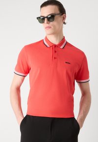 Rød polo skjorte med kontrasterende svart og hvit stripet krage og mansjetter, med en tre-knappers placket og liten brodert logo.
