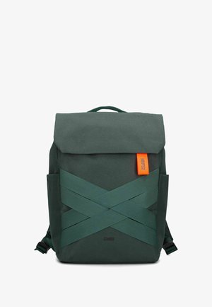 Mochila verde con cierre de solapa, que presenta correas gruesas entrelazadas y una etiqueta de acento naranja. Fabricada con un tejido resistente y texturizado.