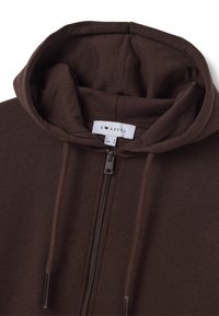 Sudadera marrón con cremallera y capucha forrada, cordones ajustables y una textura de tela suave. La etiqueta muestra "B ♥ ANGEL" con detalles de tamaño.