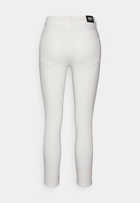 Jeans brancos skinny com uma textura suave, apresentando uma cintura alta e dois bolsos traseiros. A etiqueta da marca é visível na cintura.