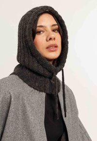 Sciarpa a cappuccio grigio scuro a coste con lacci, abbinata a un cappotto grigio chiaro a trama, dotato di chiusura con zip e un distintivo rotondo.