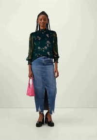 Blusa floral verde com mangas transparentes, saia de ganga azul com uma fenda frontal, sapatos plataforma pretos e uma pequena bolsa rosa.