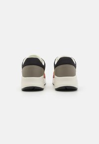Black and beige athletic shoes with a textured upper, padded collar, and contrasting red accents, featuring a white sole and rubber tread.