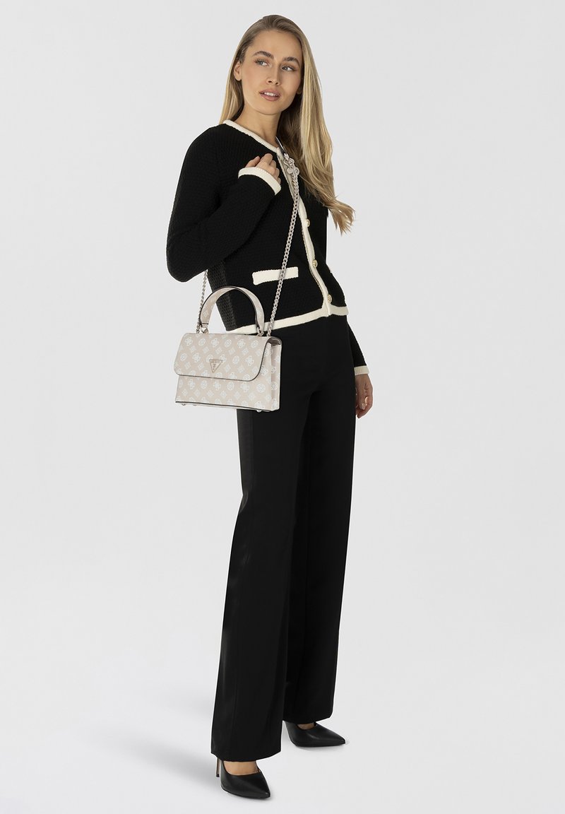 Cardigan nero con bordi bianchi, bottoni dorati; borsa crema con motivo logo e tracolla in argento; modella che indossa pantaloni neri e tacchi.