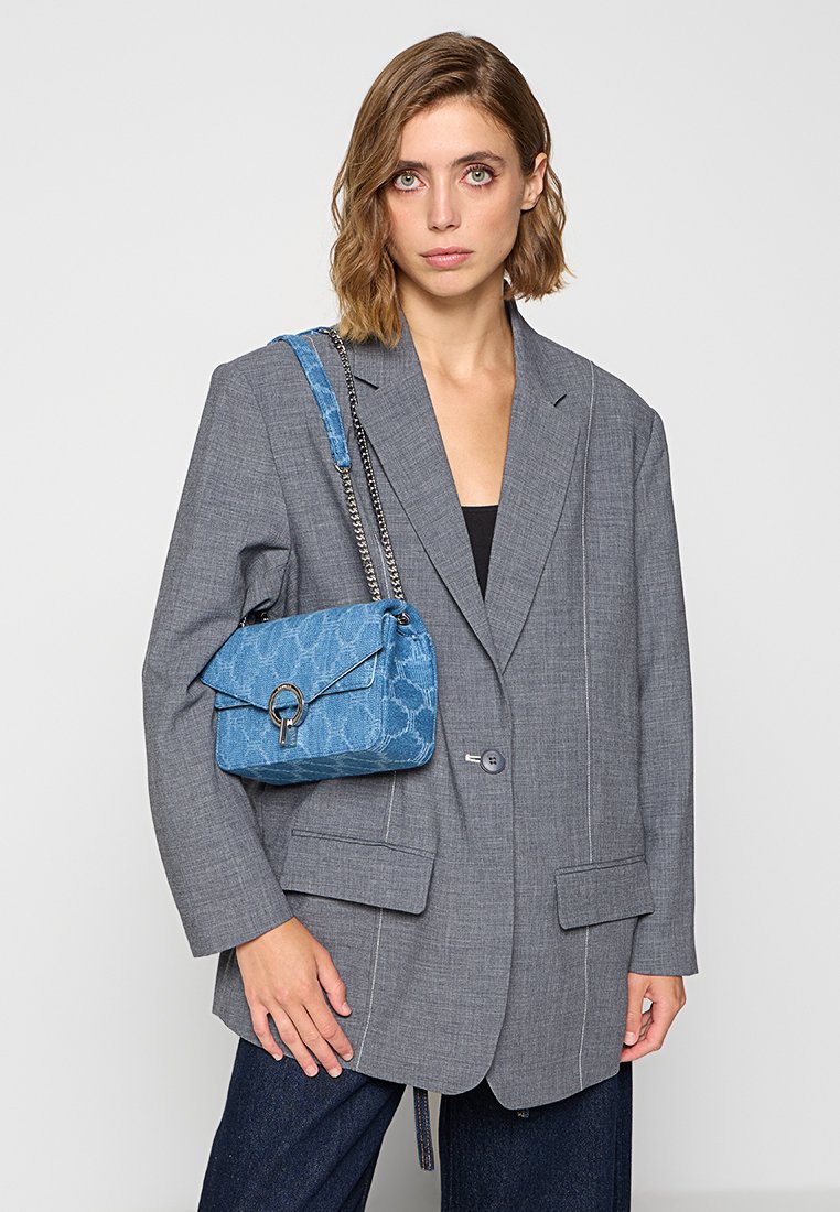 Blue textured handbag with a patterned finish, silver hardware, and chain strap, paired with a gray oversized blazer and dark pants.
