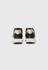 Black athletic shoes with metallic gold accents, textured fabric upper, and thick white midsole. Features a rounded toe and padded collar.