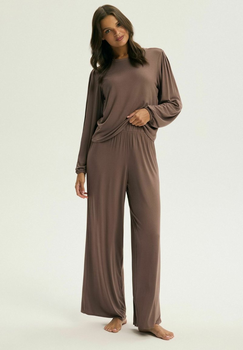 Brązowy zestaw składający się z długiego rękawa oraz spodni z szerokimi nogawkami, wykonany z miękkiego materiału. Posiada marszczone detale przy rękawach oraz elastyczny pas dla komfortu.