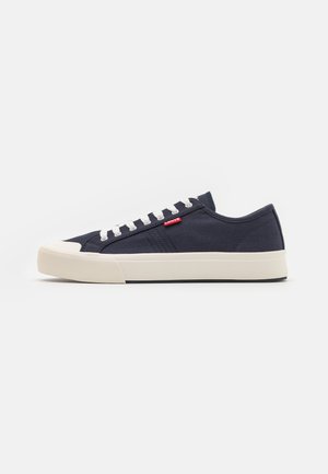 Sneakers in tela blu con punta in gomma bianca, lacci bianchi e dettagli del logo rosso. Presentano un pannello laterale testurizzato e una suola piatta.