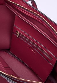 Interno di una borsa in pelle bordeaux con cerniera dorata, molteplici scomparti e una piccola tasca con zip. Materiale texturizzato e cuciture a contrasto.