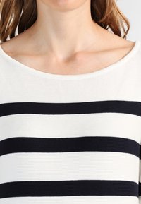 Biały i granatowy sweter w paski z szerokim dekoltem. Materiał ma teksturowane wykończenie, z wyraźnymi poziomymi pasami.