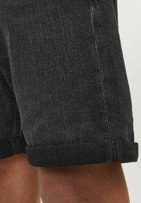 Shorts en denim noir avec un ourlet roulé, présentant une texture lisse et un léger dégradé de couleur. Coutures visibles le long des coutures.