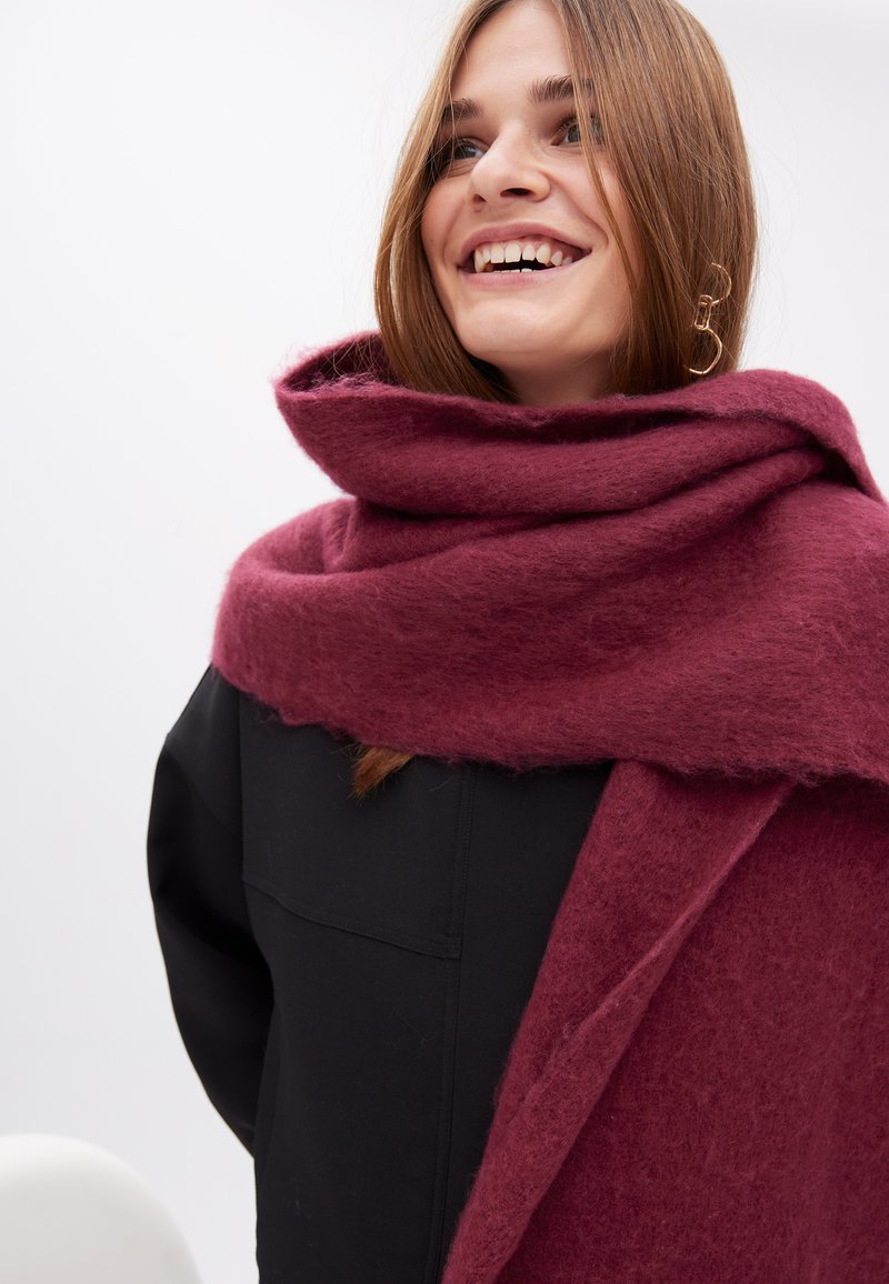 Mørkerød uld tørklæde med en blød, tekstureret finish, der er viklet omkring halsen. Har et tykt, hyggeligt design og hænger elegant.