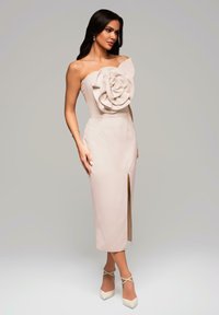Nehmotná šaty bez ramínek s velkým květinovým detailem z látky na hrudi, tužková silueta a rozparek ke stehnům. Akcentováno světlými podpatky.