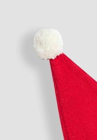 Punane kudumüts Santa stiilis, millel on pehme valge pom-pom tipus, heledalt halli tausta ees.