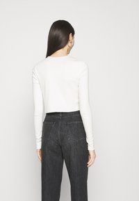 Cropped, long-sleeve top in soft white fabric; features a round neckline and a clean design. Paired with high-waisted dark jeans.