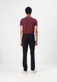 Burgundy polo shirt with white collar and sleeve trim, paired with black slim-fit trousers. The shoes are beige with a textured finish.
