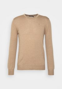 Pull beige à manches longues en tissu doux. Il présente un col rond et un petit logo sur la poitrine gauche. Poignets et ourlet simples en tricot côtelé.