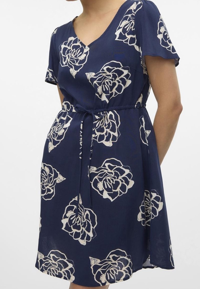 Robe bleu marine avec un col en V, des manches courtes, une taille nouée et un motif de roses blanches sur un tissu léger. Ourlet évasé.