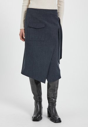 Donkerblauwe wikkelrok van gestructureerde stof met een zijstrik en een zak op het voorpaneel. Draagt goed in combinatie met kniehoge zwarte leren laarzen.