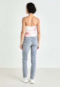 Hvit tube top med rosa blomstermønster kombinert med lyseblå høytlivsjeans og hvite joggesko. Glatt tekstur, tettsittende design.