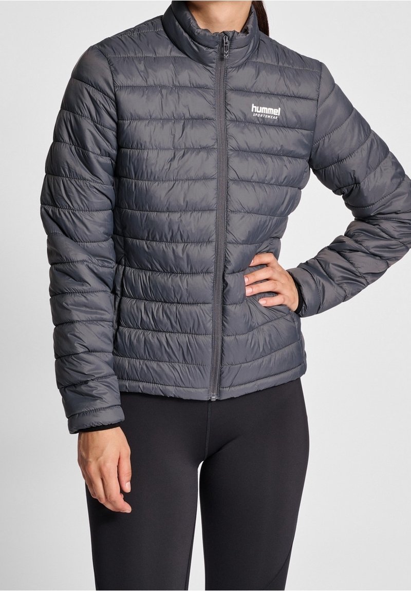 Veste matelassée grise avec col montant et fermeture à glissière. Fabriquée en matériau léger et brillant avec des coutures visibles et un détail de logo.