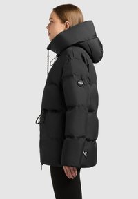 Crna puffer jakna s visokim ovratnikom, prevelikim dizajnom, rukavima s manžetama i oznakom logotipa na ruci. Uključuje podešavajuće vezice.