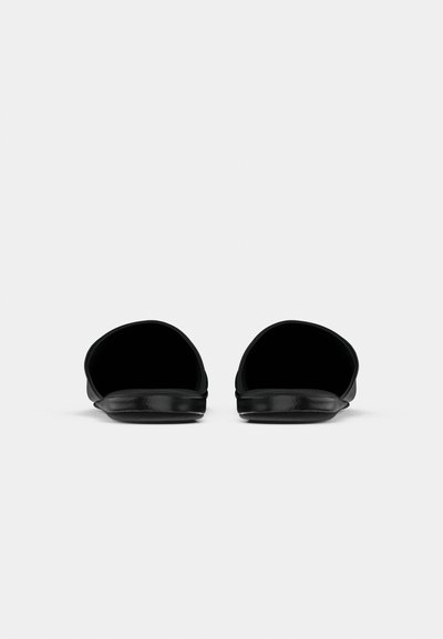 Une paire de sandales ouvertes noires avec des semelles brillantes, présentées de face sur un fond blanc uni.