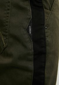 Gröna och svarta cargo-byxor med en slät yta, sidofickor och en märkesetikett sydd på sömmen.